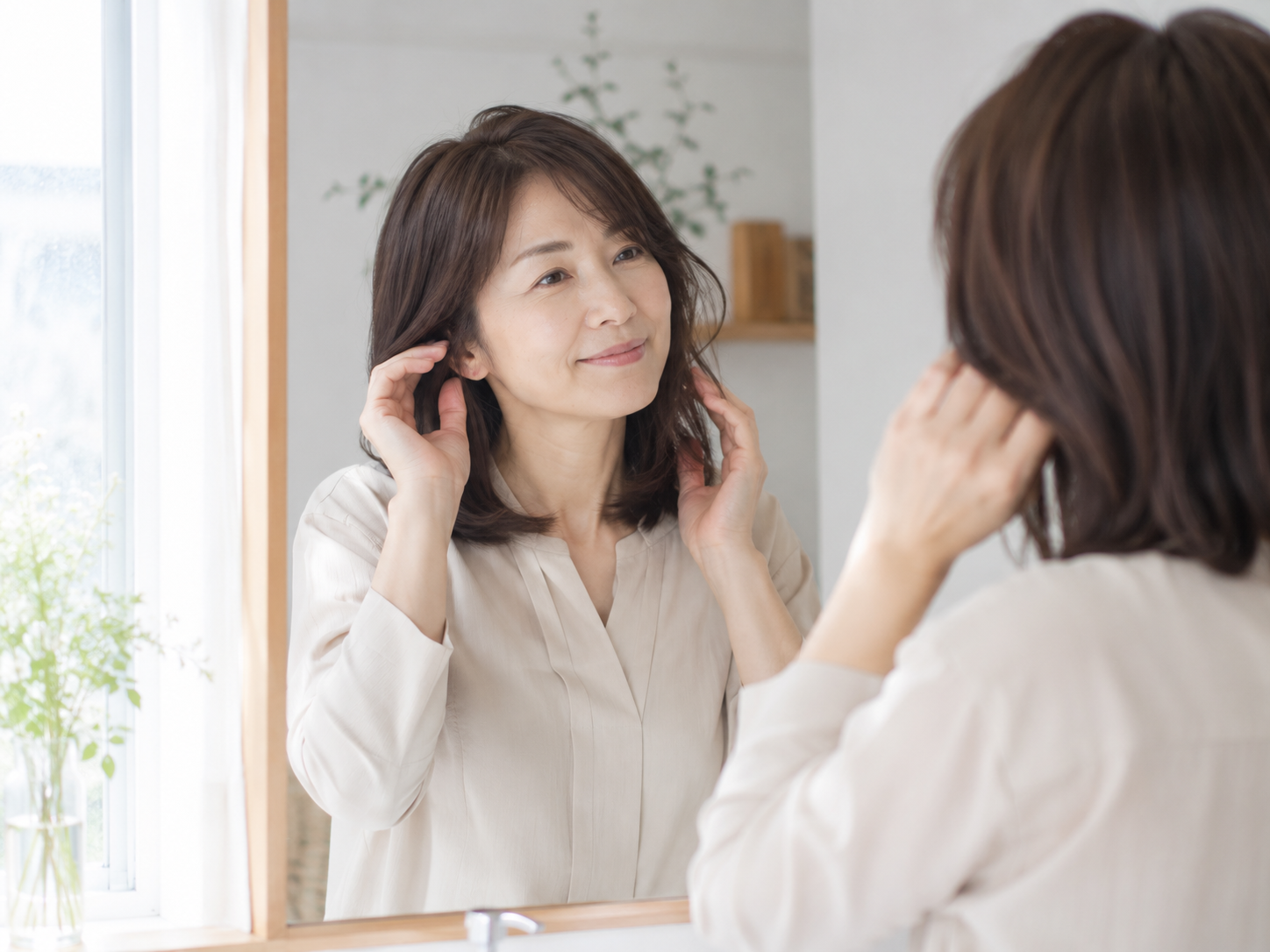 朝の鏡の前で髪を整える40〜50代女性。毎日のスタイリングが少し楽しくなるような自然な雰囲気が伝わる写真。