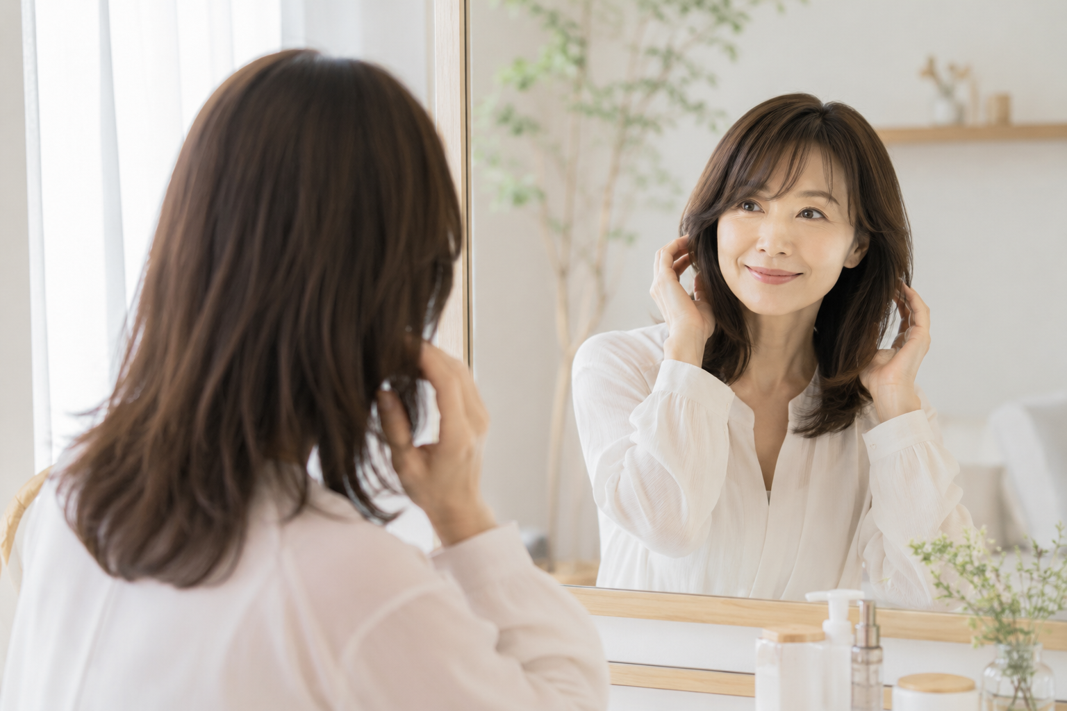 朝の鏡の前で自然に髪を整え、乾かすだけでまとまる髪を楽しむ40〜50代女性の生活シーン。
